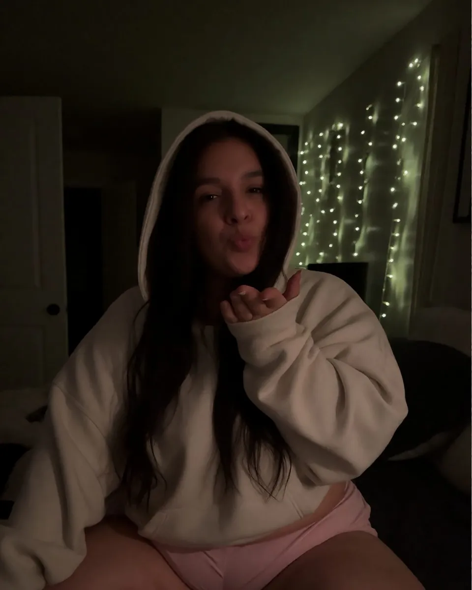Catlina le soir chez elle, sweat à capuche crème, guirlande lumineuse au mur