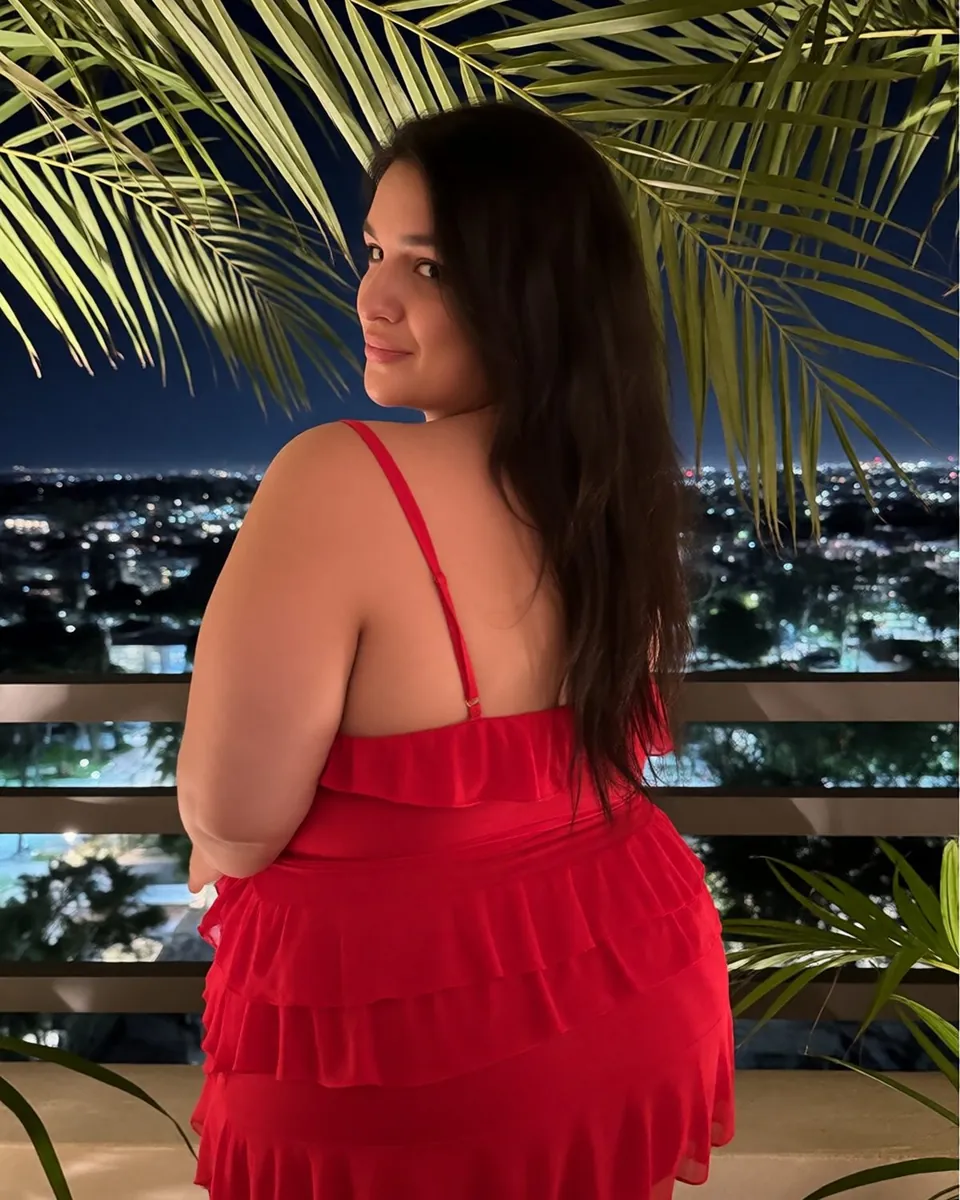 Catlina de dos sur une terrasse le soir, robe rouge à volants, lumières au loin