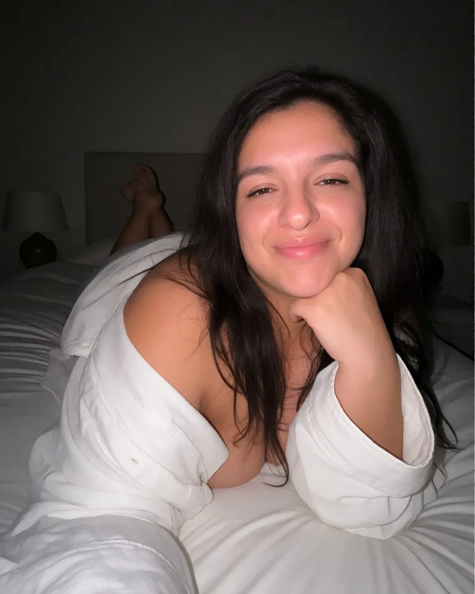 Catlina allongée sur un lit blanc, chemise blanche, menton posé sur la main