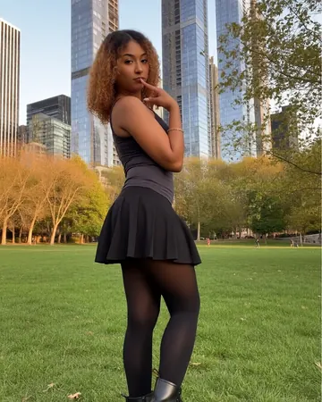 Emma en un parque bajo los rascacielos, pelo rizado, falda negra y botas