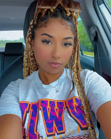 Emma taking a selfie in a car, long blonde braids, printed t-shirt