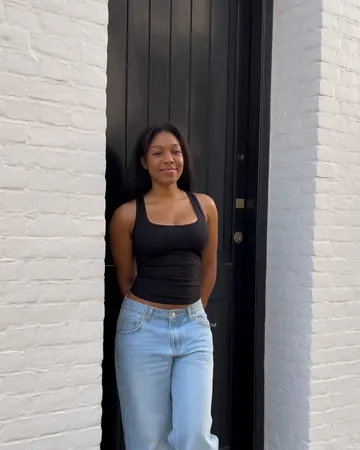 Maya in a black doorway, black tank top and light jeans