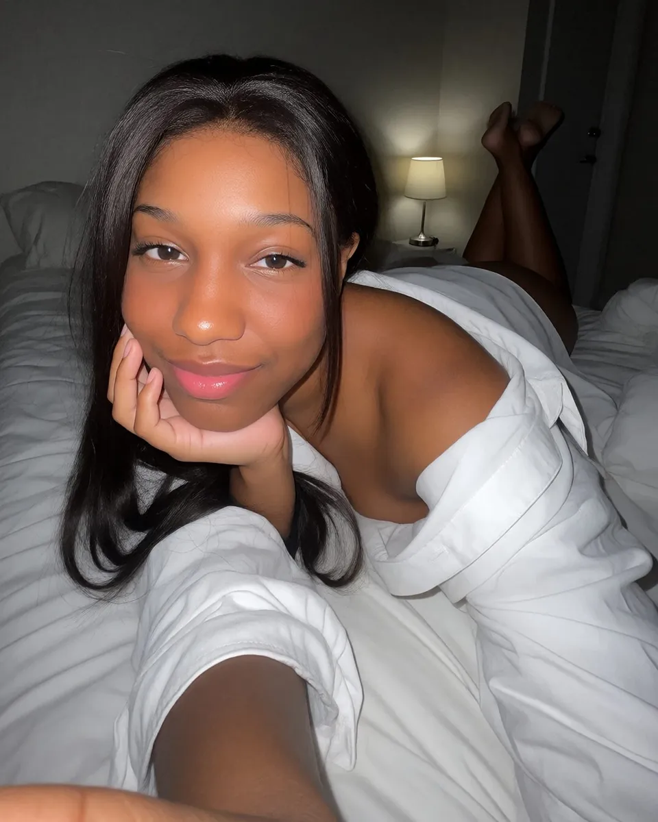 Maya lying on a white bed, white shirt, chin in her hand
