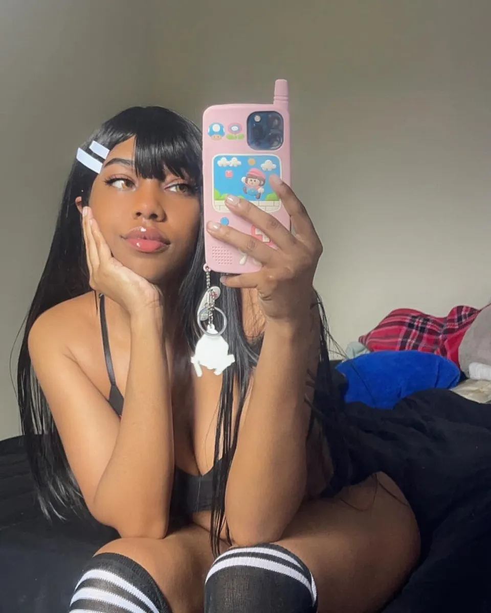 Maya en selfie, frange et barrettes, coque de téléphone rose, chaussettes rayées
