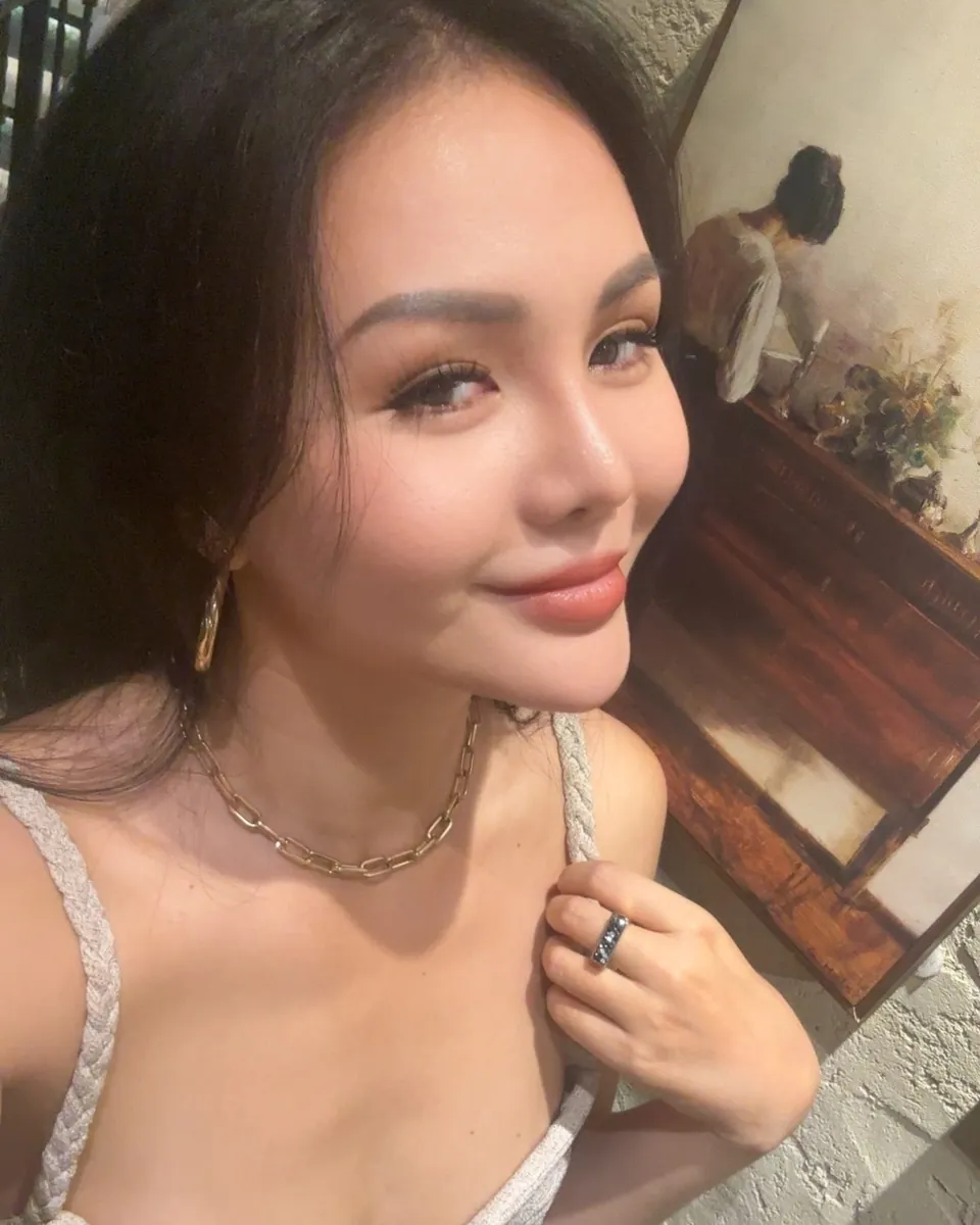 Mia en selfie à l'intérieur, sourire, collier doré et débardeur clair