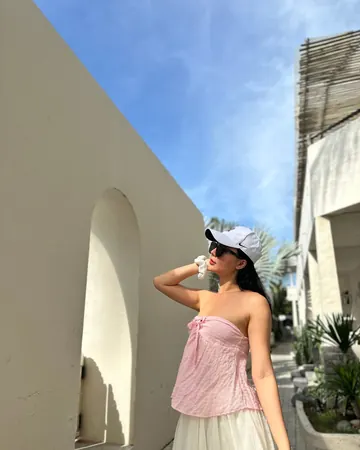 Mia in a white cap in a light-walled alley, pink top and tulle skirt