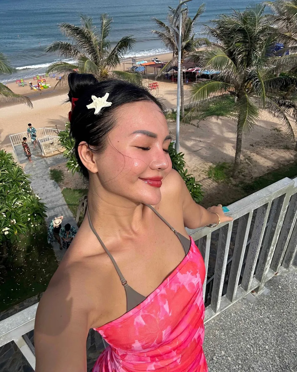 Mia sur un balcon face à la plage, pince étoile de mer dans les cheveux, robe rose fleurie