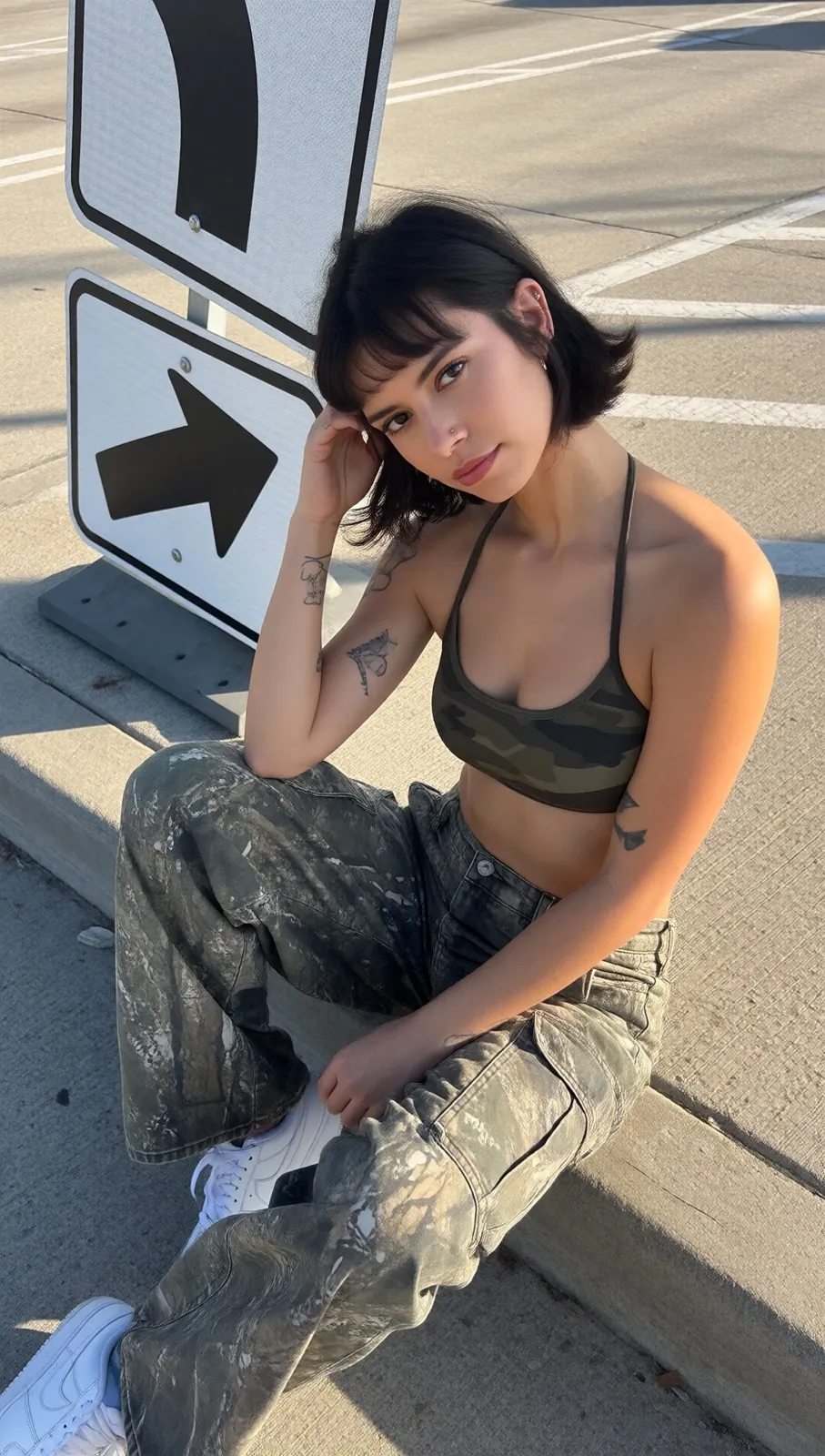 Romy assise sur un trottoir près d'un panneau, haut et pantalon camouflage