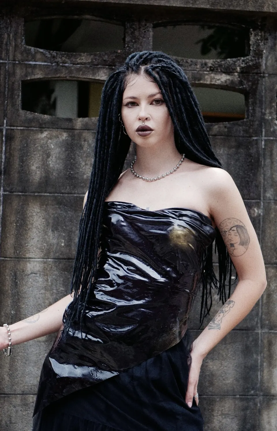 Vera devant un mur de pierre, haut noir brillant, longues tresses noires